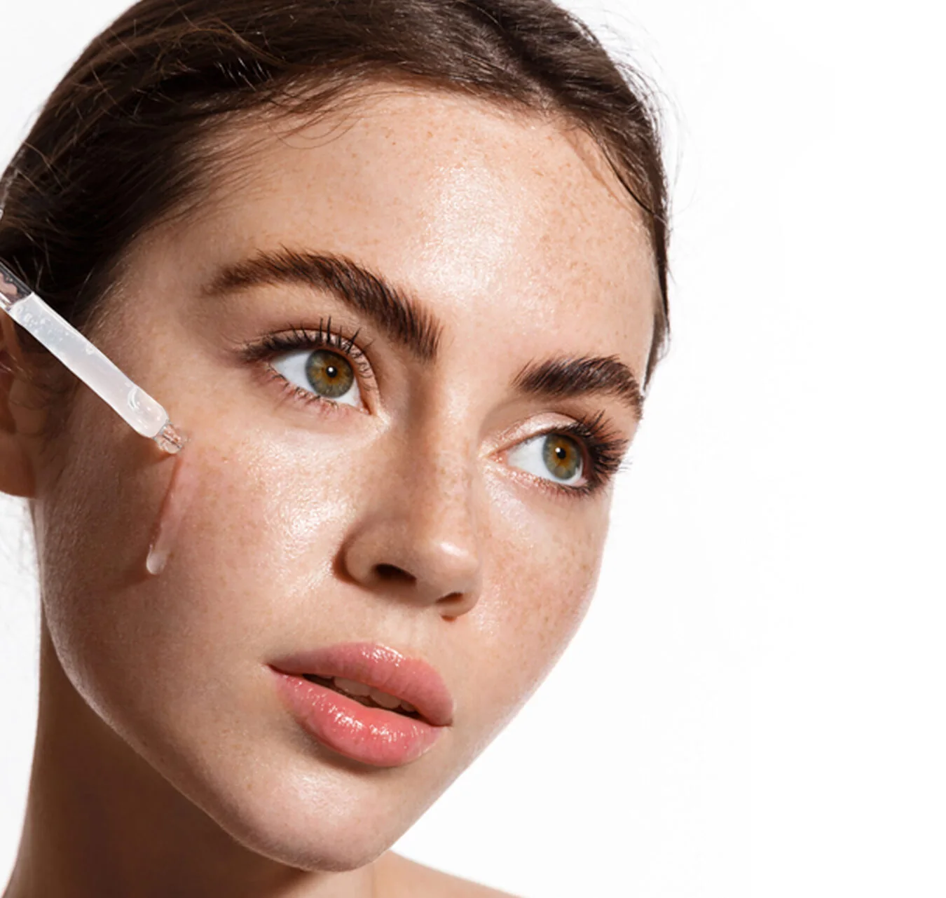 A dropper of serum held against a cheek