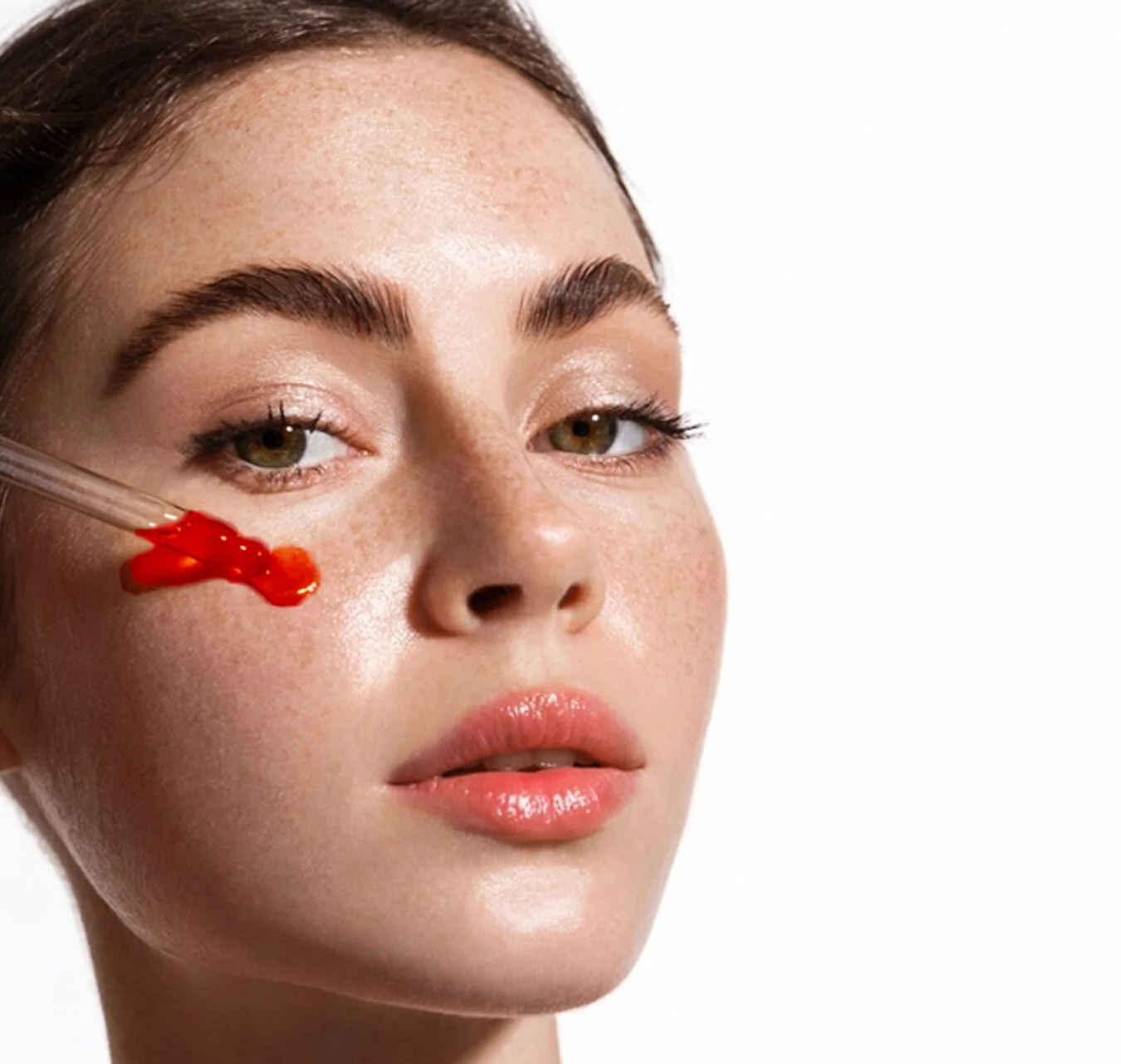 A dropper of serum held against a cheek